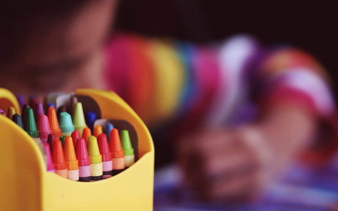 a child coloring with a bright box of crayons