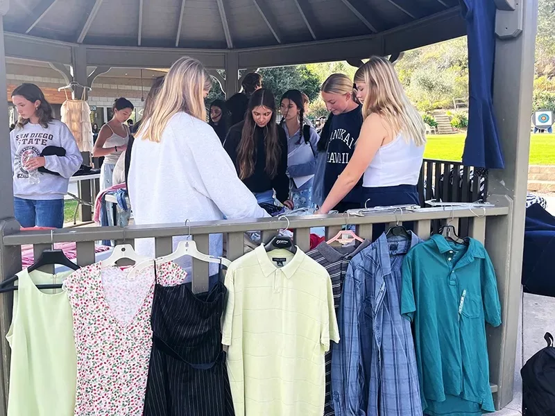 Photo showing high school girls outside with shirts hanging on a rack.