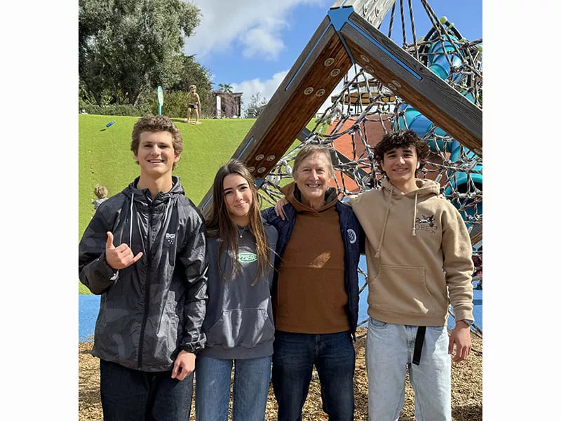 Dr. Stuart Grauer posing with 2 high school males and 1 high school female for a photo smiling at the camera on a playground