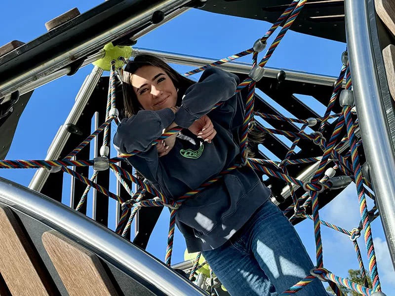 High school girl on a playground with her arms leaning on a chain and smiling at the camera