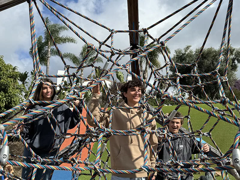 High school girls and boys climbing a rope web on a playground