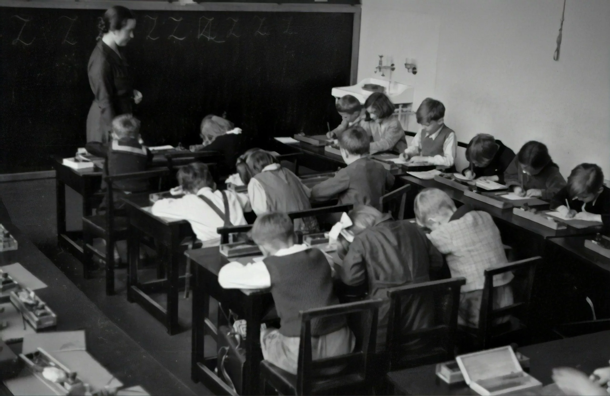 A black and white photo of a teacher giving a handwriting lesson to students