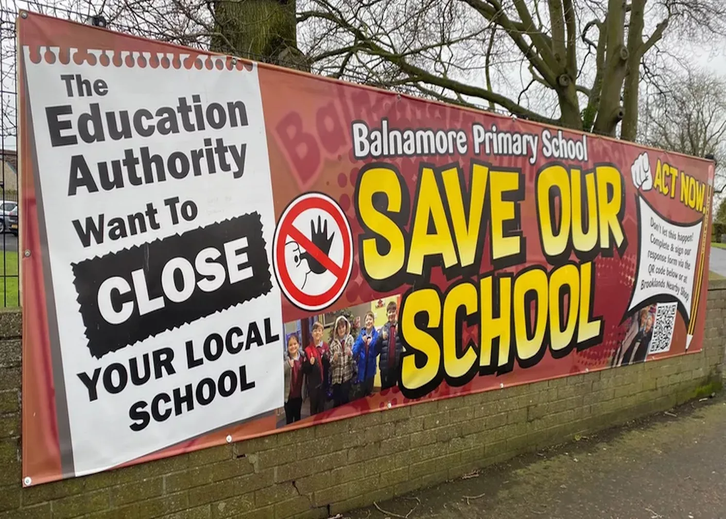 Photo of a sign that says Save Our School displayed on a fence with trees in the background