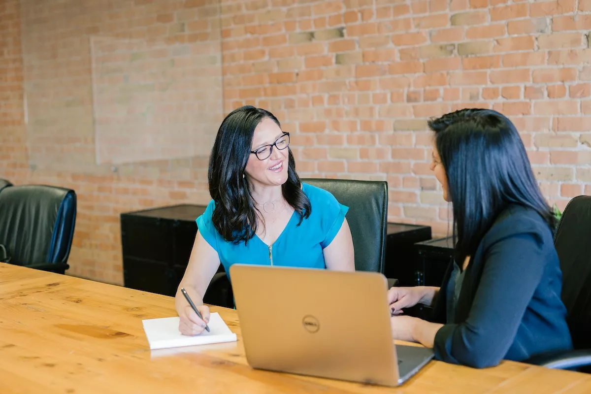 Two adults talking and engaging in dialogue at a table with a laptop and notepad