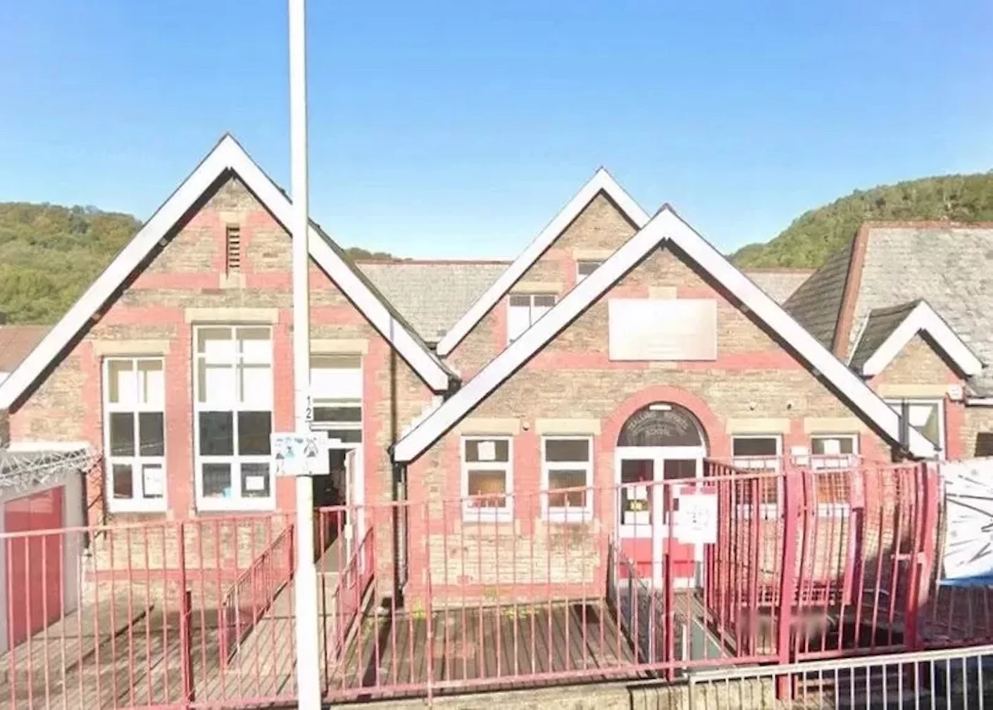 A paper sign with painted handprints with text that reads "2 schools 1 family"